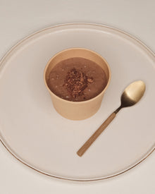 A single TSCS cup on a ceramic plate beside a spoon