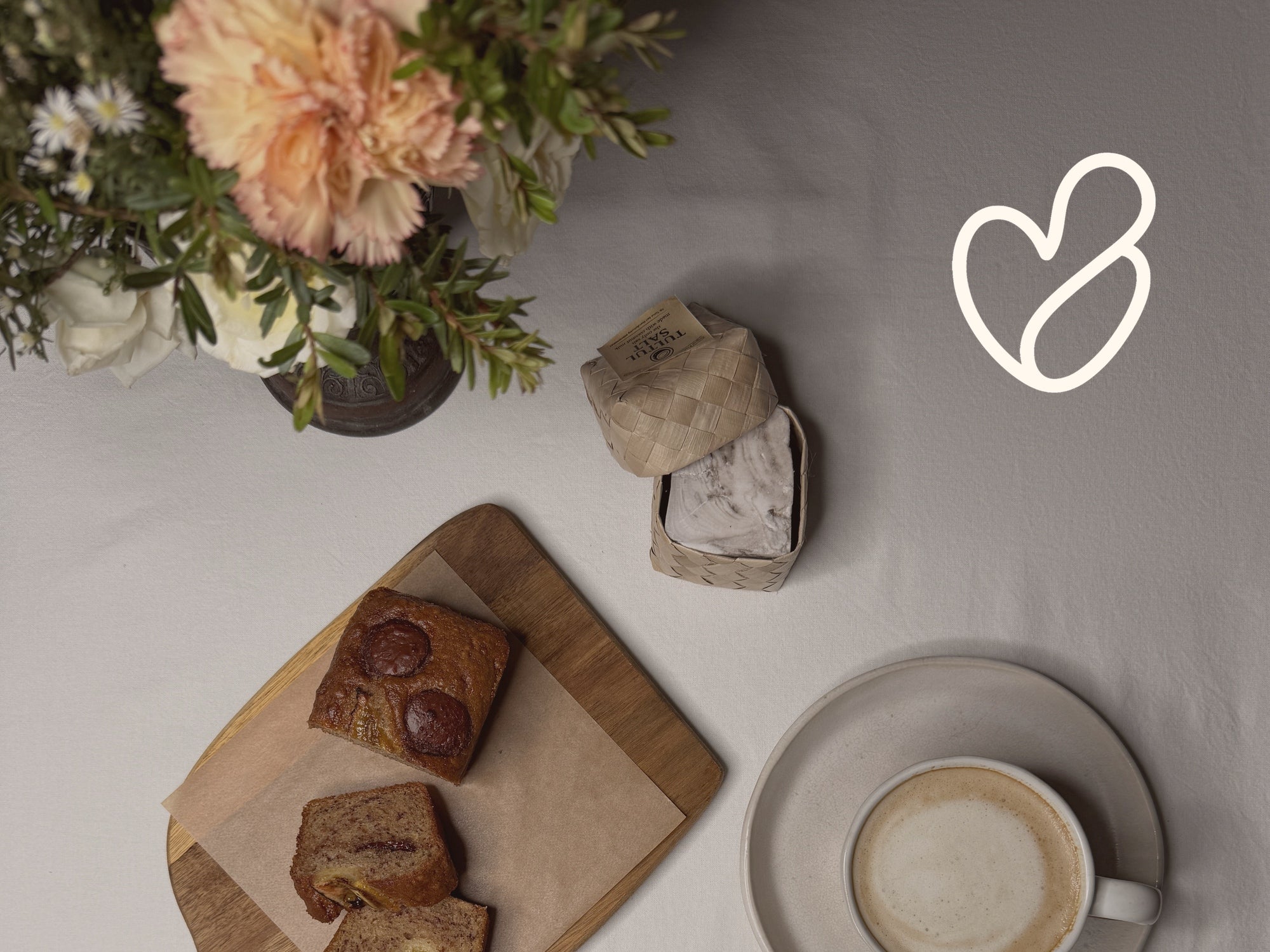 A softly set kitchen table with flowers, bread, salt and coffee